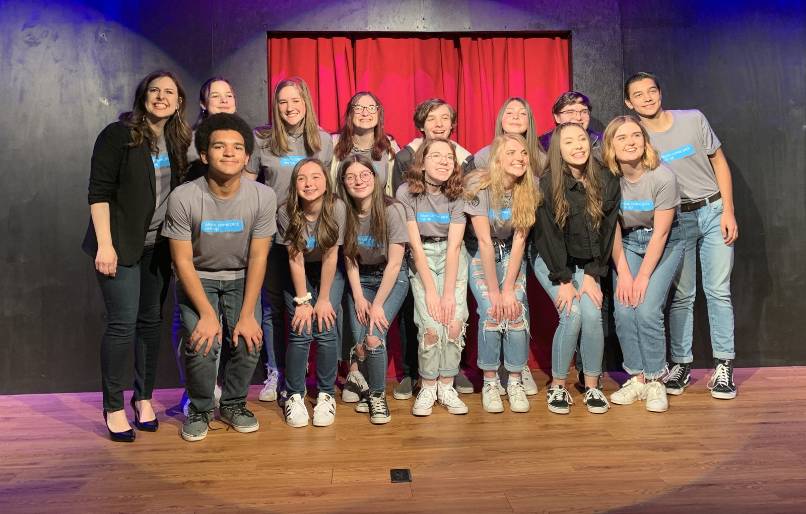 A large group of teen improv students on stage, all wearing shirts that read Mom come pick me up